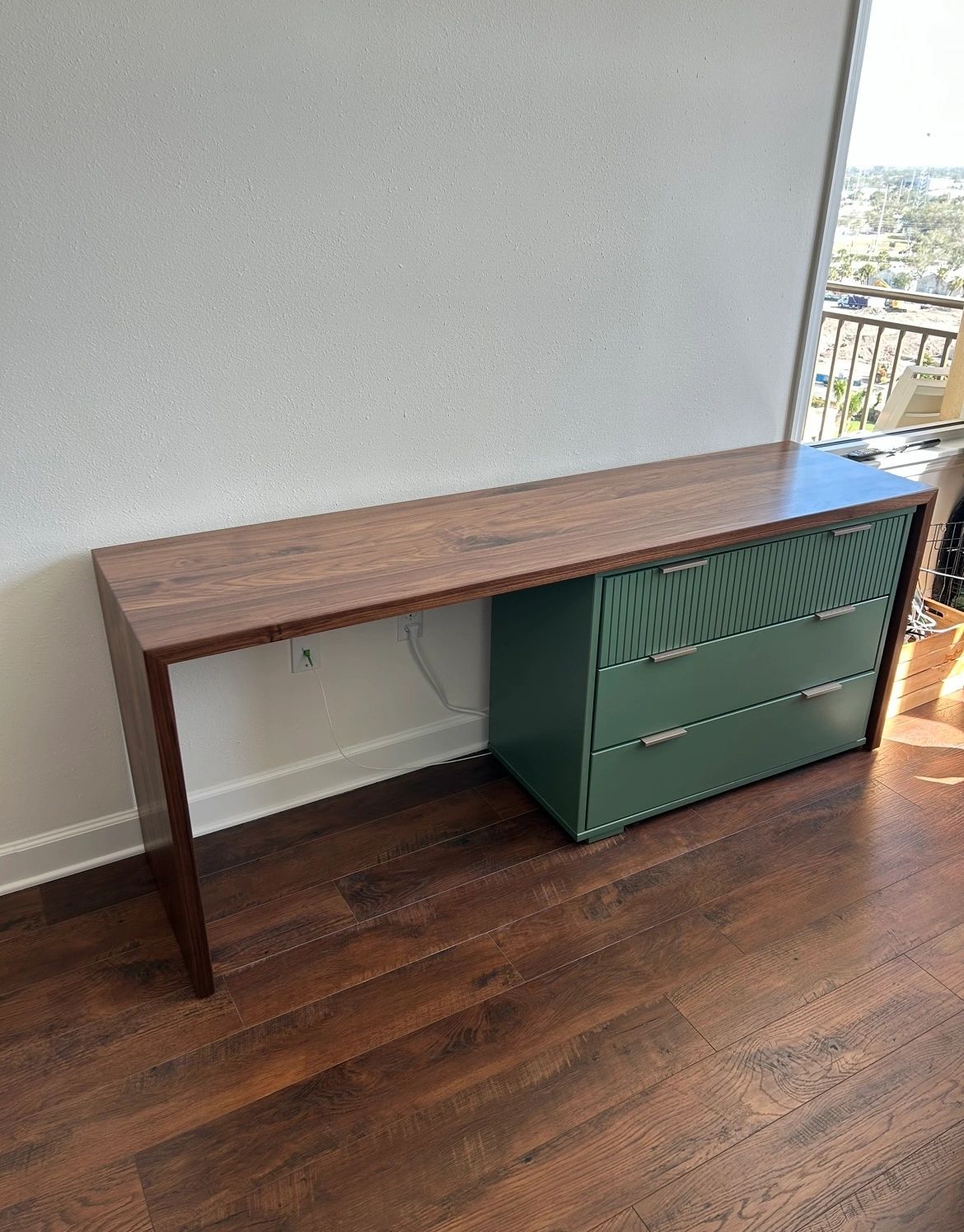 Slim walnut waterfall desk next to green cabinets
